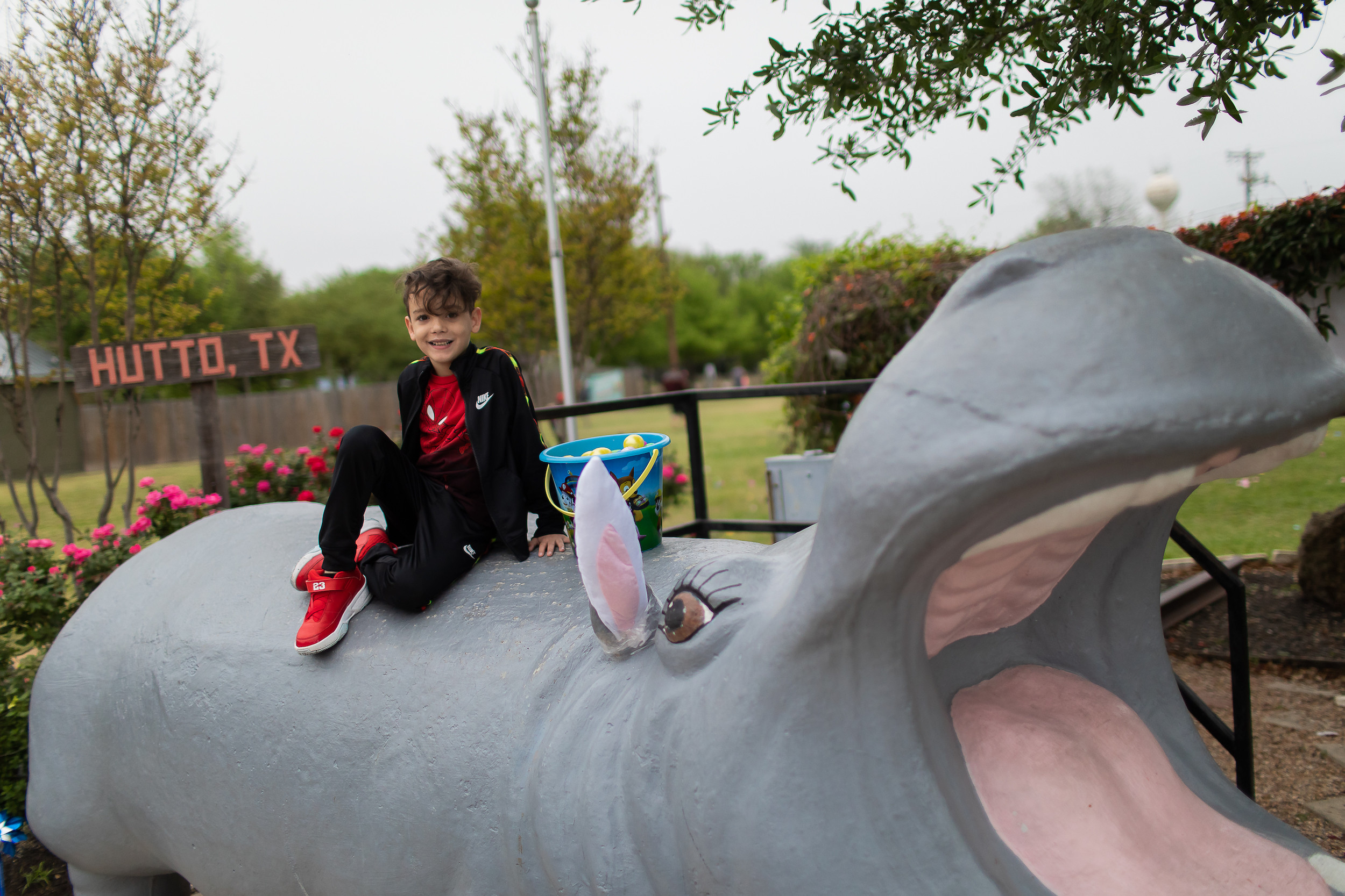 Photo of a child sitting with an Easter basket on a large concrete hippo with a Hutto, TX sign in the background