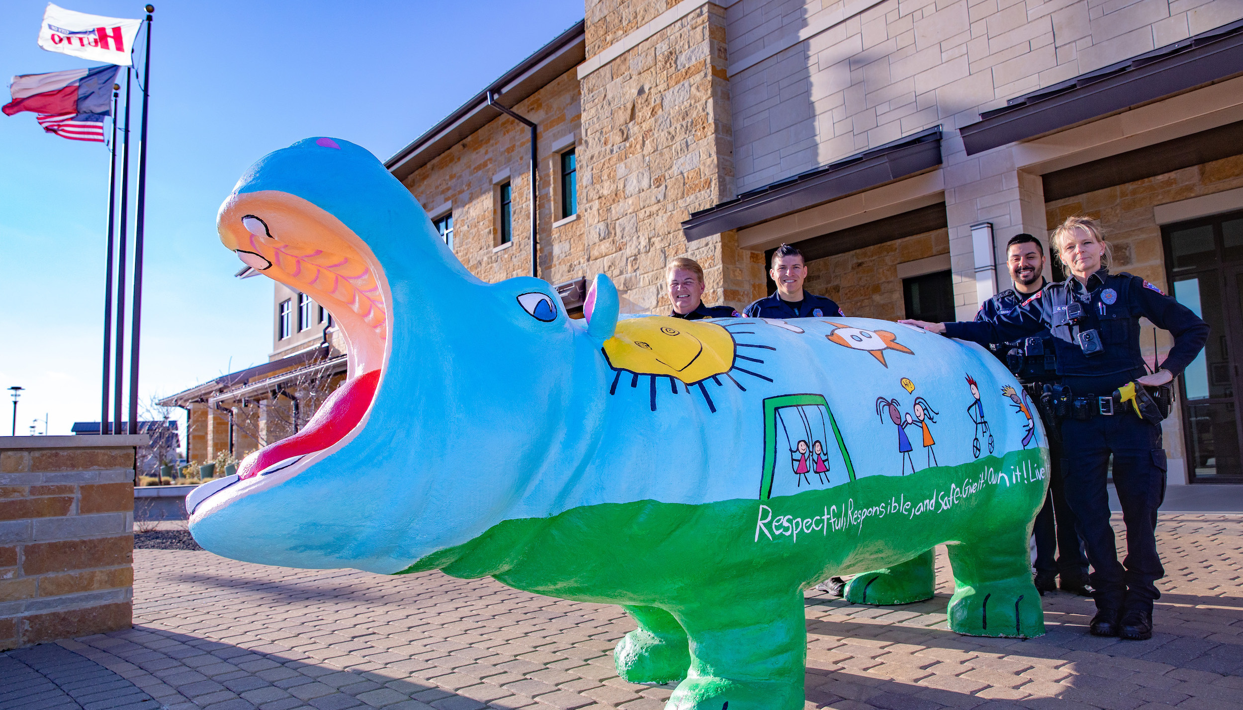 Photo of police officers standing with a concrete hippo painted with children playing outside